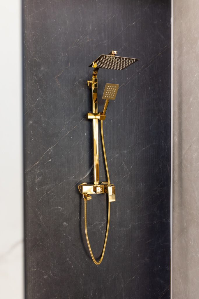Luxuriöse goldene Regendusche in modernem Badezimmer mit dunkler Steinoptik.